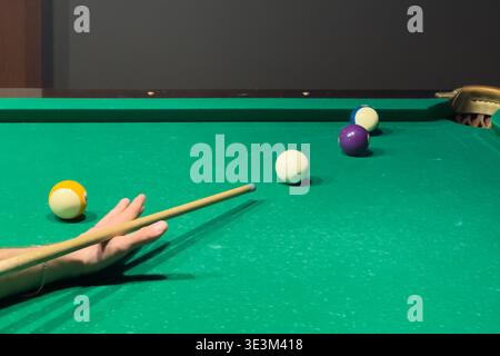 A close-up view of a billiard table with colored balls arranged on green felt. Cue in hand suggests preparation for a strategic shot in a leisure acti Stock Photo