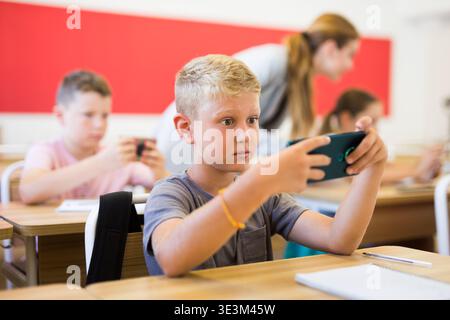 Absorbed preteen boy using smartphone at lesson in school Stock Photo