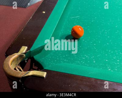 A close-up of a billiard table shows a red ball near the edge on green felt. The wood details are visible with natural light adding to the scene of ga Stock Photo