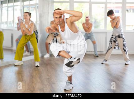 Young man together with group of teenage students, learn to dance hip hop in choreographic hall Stock Photo