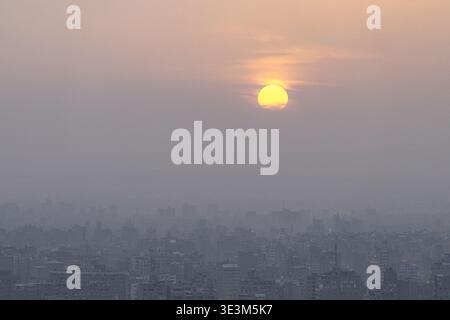 View of the sun piercing through the hazy sky above the cityscape, casting a warm glow over the buildings below, Cairo, Cairo Governorate, Egypt. Stock Photo
