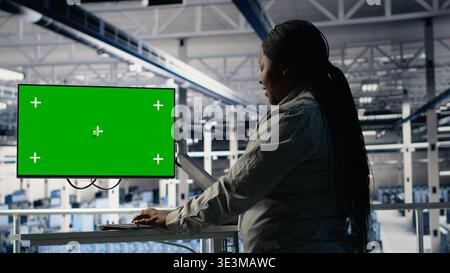 Software developer in server hub using chroma key workstation to scan equipment for issues. African american woman in data center uses isolated screen PC to do backups, camera B Stock Photo