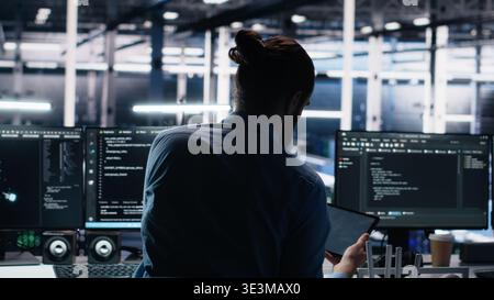 Admin using devices in data center, coding with generative AI assistance. IT employee oversees leveraging artificial intelligence large language model tech on PC, laptop and tablet, camera A Stock Photo