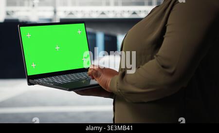 Data center expert monitors data center metrics on isolated screen laptop to enhance operational effectiveness. Server hub worker uses analytics on mockup notebook to predict performance, camera B Stock Photo