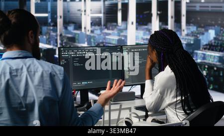Data center coworkers having fun in office, using machine learning algorithms to analyze datasets. Server farm colleagues goofing around while using AI at work, workplace friendship concept, camera A Stock Photo