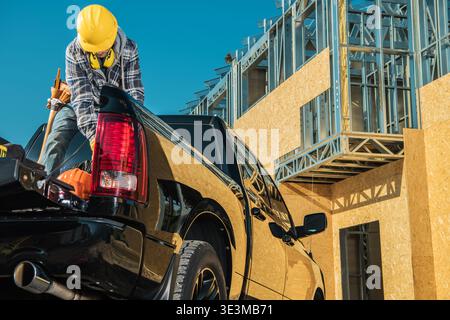 A construction worker loads tools into a truck at a building site on a sunny day. Stock Photo