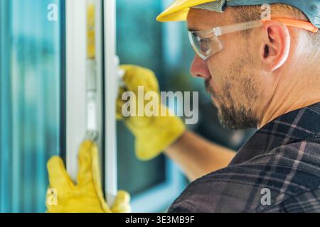 A worker focuses on installing a window frame in a building. Safety gear is visible. Stock Photo