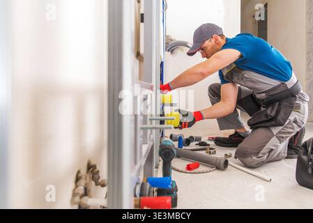 A plumber is installing pipe fittings and checking tools on the floor in a building. Stock Photo