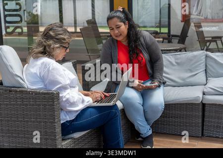 Women discussing business using laptop and smartphone outdoors in a casual setting Stock Photo