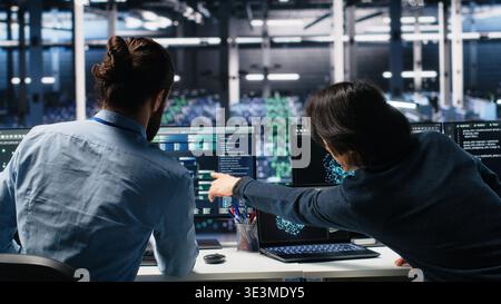 Data center admins doing brainstorming, working on neural network software development. Server farm IT employees working together, implementing machine learning technology using PC, camera A Stock Photo