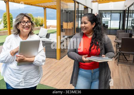 Two smiling businesswomen interacting while walking through a modern outdoor office space Stock Photo