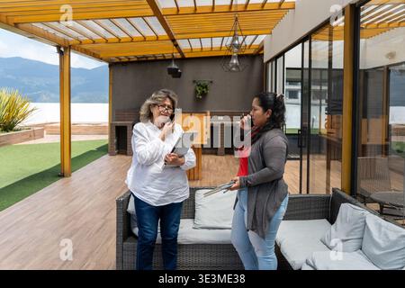 Women talking on cell phones and carrying a laptop on a modern rooftop terrace Stock Photo