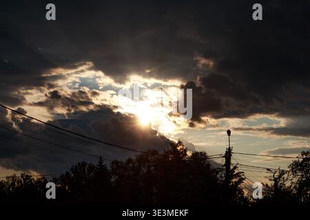 Majestic sunlight pierces through stormy clouds, creating a dramatic sky at dusk. Golden rays peek through dark, thick cumulonimbus Stock Photo