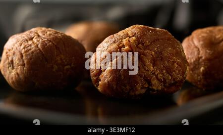 round balls of dark brown jaggery on dark surface, unrefined cane sugar in soft focus, natural sweeteners and south asian ingredients concept Stock Photo