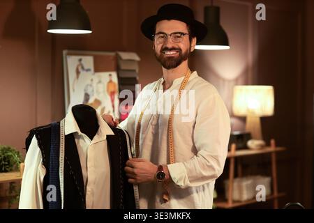 Male tailor measuring jacket on mannequin in atelier at night Stock Photo