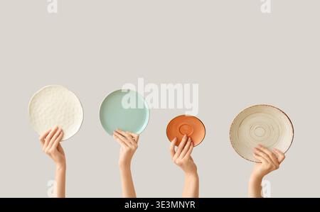 Hands holding empty plates on light background Stock Photo