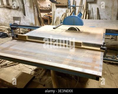 A table saw is set up in a workshop filled with wood Various pieces of wood lie on the ground The environment shows tools and equipment used for woodw Stock Photo