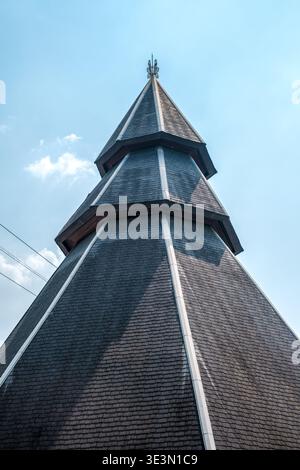 Towering wooden spire rises against clear blue sky. Shingles form intricate, layered pattern across its surface. Sharp angles and weathered texture ad Stock Photo