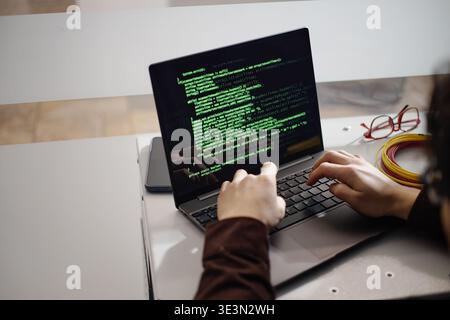 Young Adult Man Typing Code on Laptop Computer in Office Setting Stock Photo