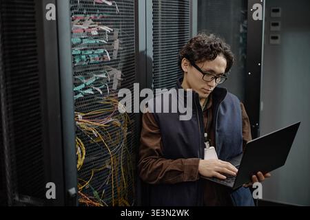 Young Adult Asian Man Using Laptop While Working Inside Server Room Stock Photo
