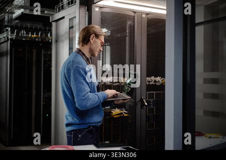 Middle Aged Caucasian Man Using Laptop While Monitoring Server Room Equipment Stock Photo