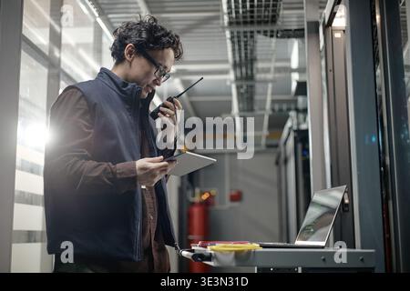 Young Adult Asian Man Using Walkie Talkie While Working in Server Room Stock Photo