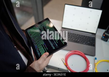 Young Adult Man Holding Tablet Displaying Code near Laptop Working Stock Photo