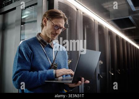 Caucasian Adult Man Using Laptop While Working in Data Center Server Room Stock Photo