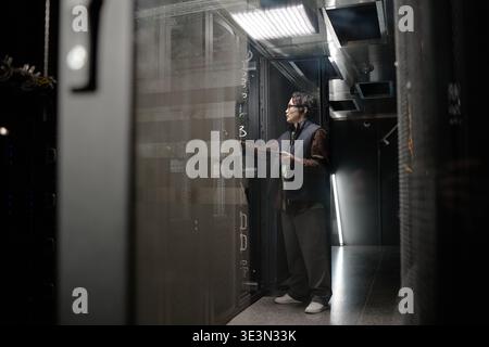 Young Adult Asian Man Troubleshooting Server Rack While Using Digital Tablet Stock Photo