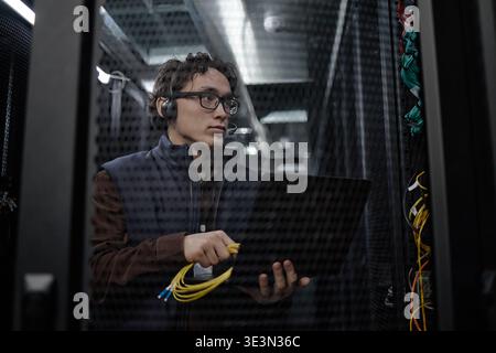 Young Adult Asian Man Working with Laptop and Network Cables in Server Room Stock Photo