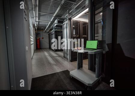 Empty Data Center Corridor Featuring Laptop on Rolling Cart near Server Racks Stock Photo