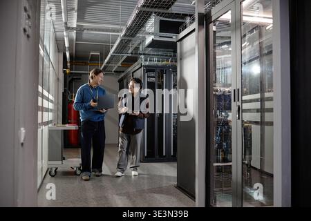 Middle Aged Caucasian Man and Asian Man Collaborating in Data Center Corridor Stock Photo