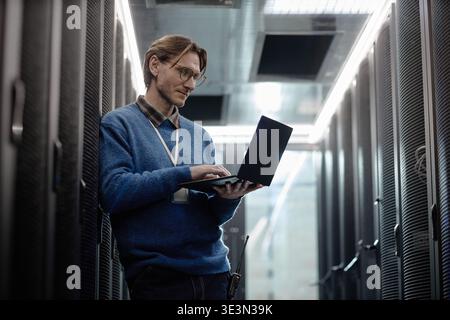 Caucasian Middle Aged Man Using Laptop While Working in Data Center Corridor Stock Photo