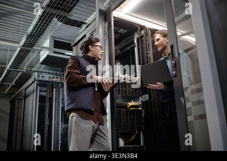 Adult Men Collaborating in Server Room While Holding Laptops and Tablets Stock Photo