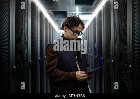 Young Adult Asian Man Using Digital Tablet in Modern Data Center Corridor Stock Photo