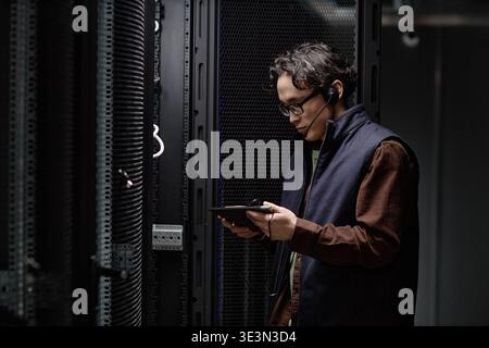 Young Adult Asian Man Monitoring Server Equipment Using Digital Tablet Stock Photo