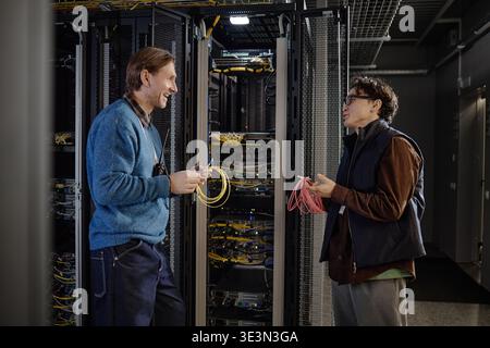 Adult Caucasian Man and Young Adult Man Discussing Network Cables in Server Room Stock Photo