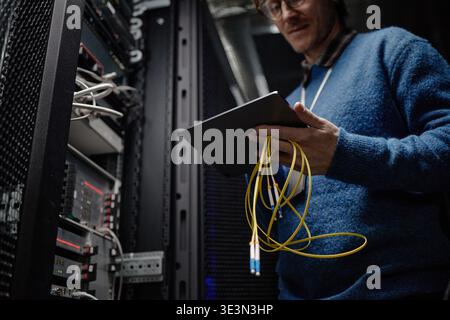 Middle Aged Caucasian Man Inspecting Server Rack While Holding Tablet Device Stock Photo