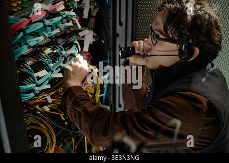 Young Adult Asian Man Troubleshooting Server Rack Wiring While Using Headset Stock Photo