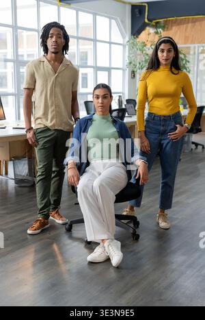 Diverse coworkers in business casual attire posing in open-plan office with computer monitors Stock Photo