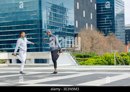 Diverse male workout partners doing quadriceps stretches on urban terrace with bench Stock Photo