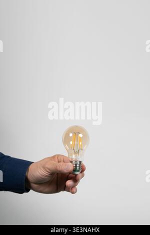 Hand holding an LED filament bulb isolated on light gray background with copy space, representing idea, innovation, energy efficiency, electricity, an Stock Photo