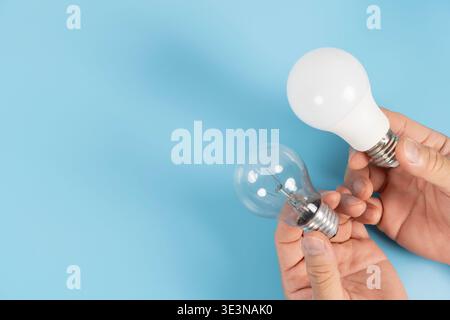 Close-up of hands holding LED and incandescent bulbs on blue background with copy space, showing energy saving, lighting replacement, efficiency compa Stock Photo