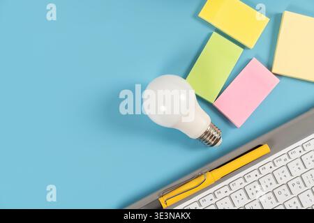 Top view of LED bulb, sticky notes, pen and keyboard on blue desk background with copy space, symbolizing ideas, planning, office work, productivity, Stock Photo
