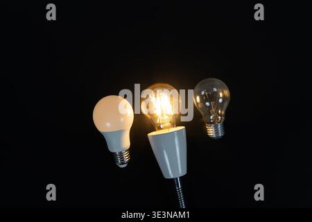 Three light bulbs on black background featuring a glowing filament bulb between LED and incandescent bulbs, symbolizing lighting comparison, energy ch Stock Photo