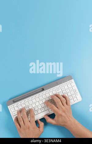 Top view of hands typing on a keyboard over blue background with copy space, ideal for office work, remote communication, digital business, content wr Stock Photo