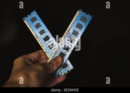 A high-angle, close-up shot of a person's hand holding two blue DDR memory sticks forming a 'V' shape. Stock Photo