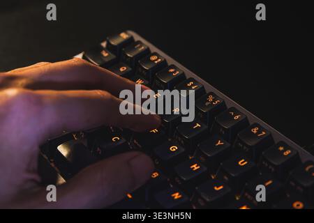 A detailed close-up shot of a person's hand pressing keys on a modern mechanical computer keyboard. The keys feature a warm orange backlight. Stock Photo