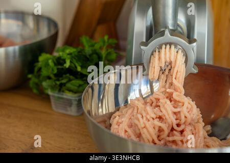 Raw chicken ground in meat grinder into bowl in kitchen. Concept: home cooking Stock Photo