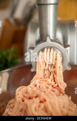 Raw chicken meat being ground in meat grinder into bowl close up. Concept: homemade food preparation Stock Photo